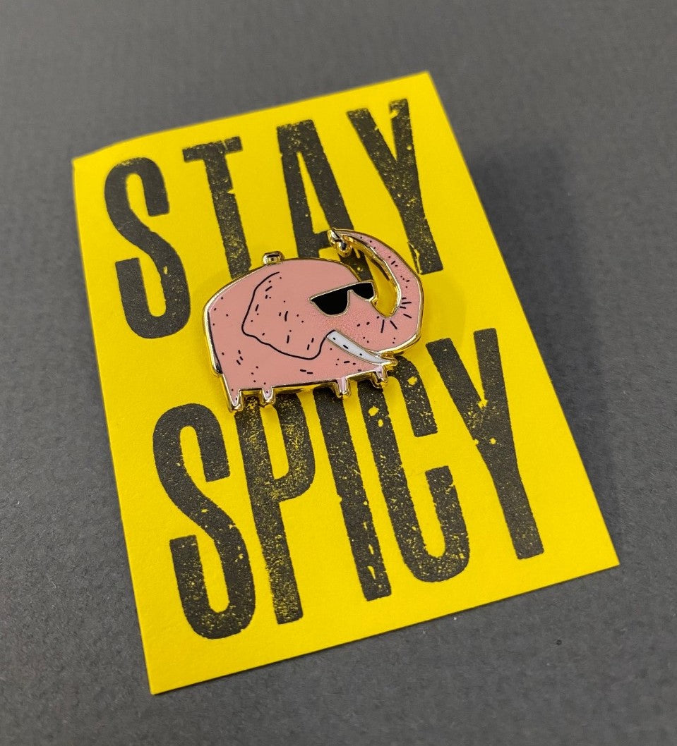 A pink elephant pin on a yellow backing that says stay spicy.